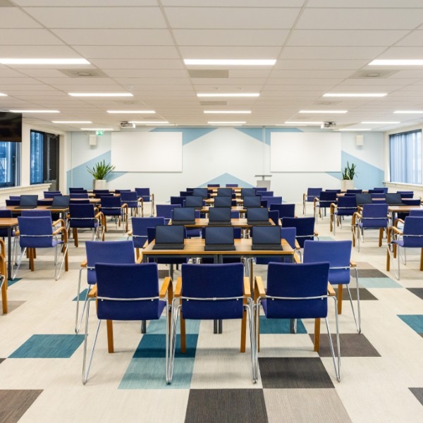 Grote zaal in Amsterdam met rijen tafels en een laptop op elke werkplek